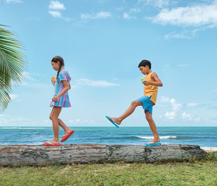 Boy and girl walking on a log on beach wearing Locals slippahs