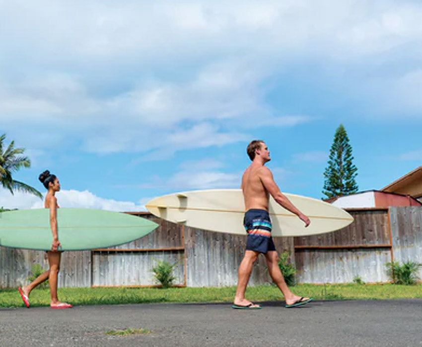 Group of surfers walking down street carrying surfboards wearing Locals slippahs