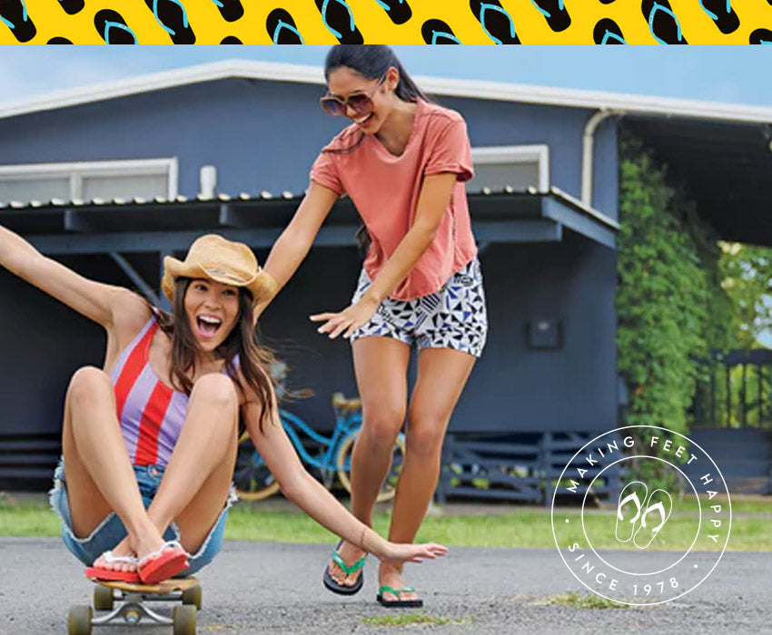 Two women playing on a skateboard wearing Locals slippahs