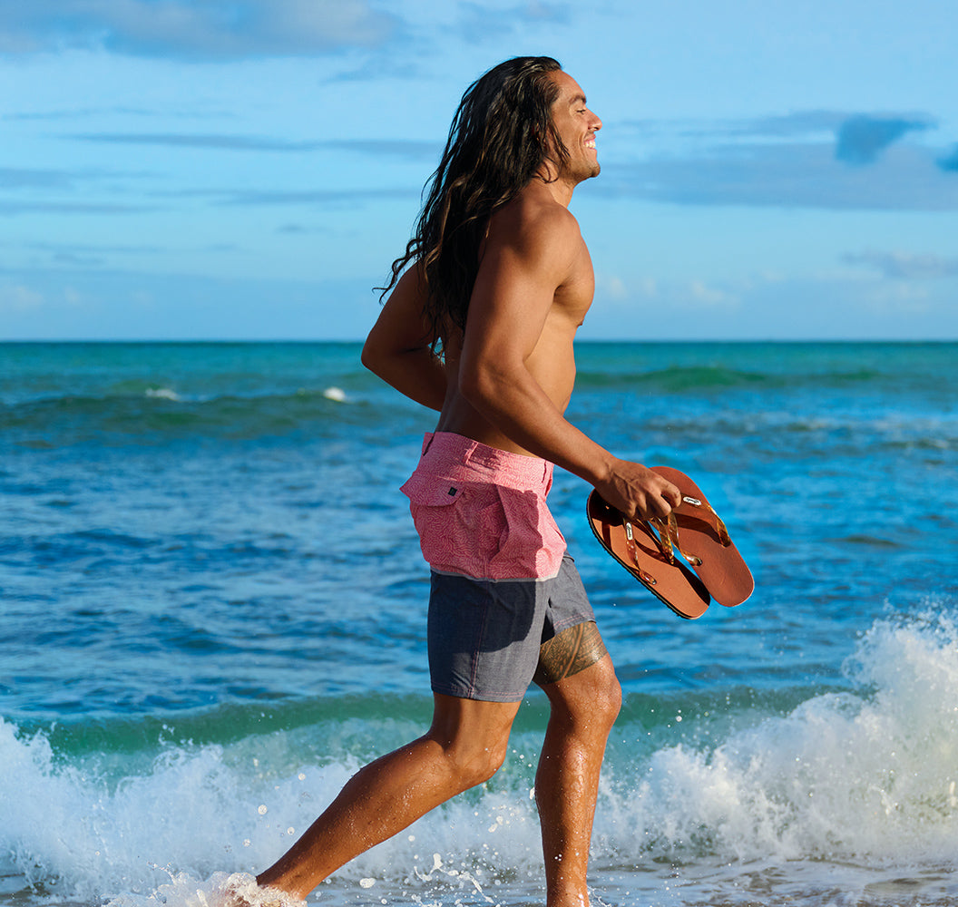 Man running on beach holding Locals slippahs