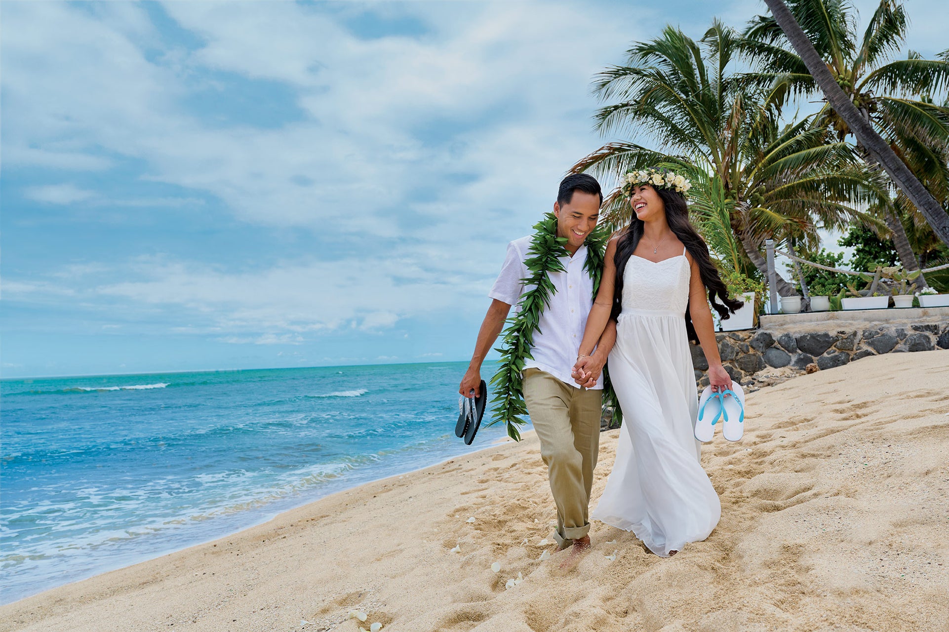 Wedding couple in white on a beach carrying Locals slippahs