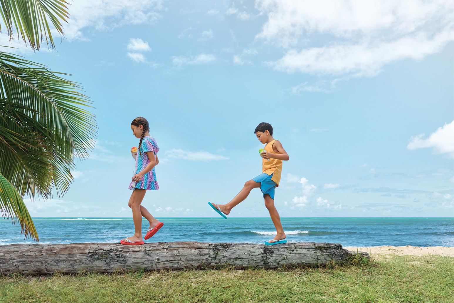 Kids walking on a log on a beach wearing Locals slippahs