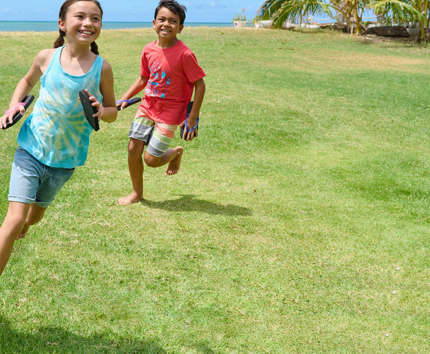 Girl and boy running in a backyard wearing Locals slippahs on hands