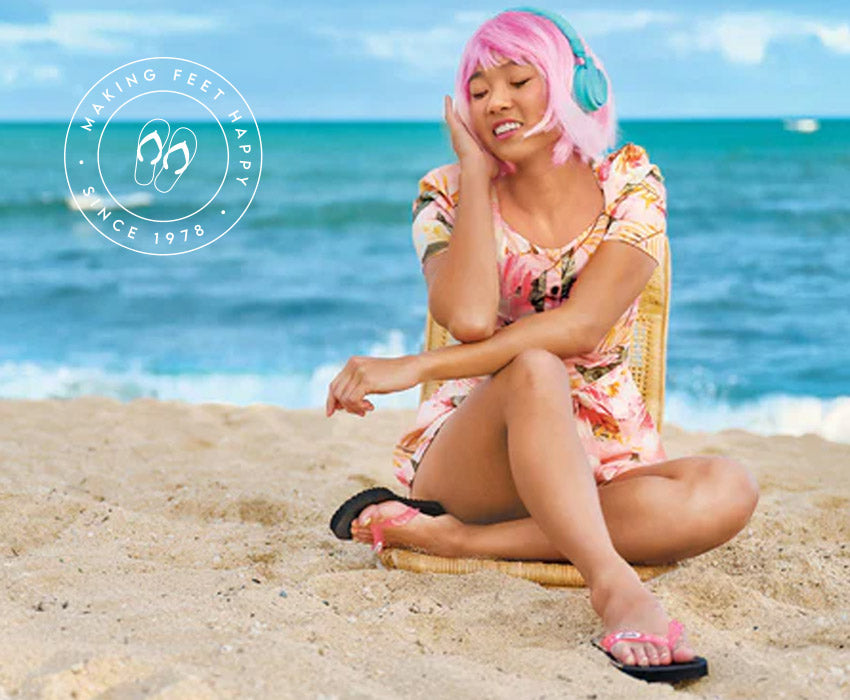 Woman with pink hair sitting on a beach wearing Locals slippahs